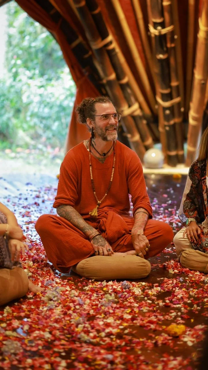 Ashton smiling while seated on a cushion beneath a bamboo roof.
